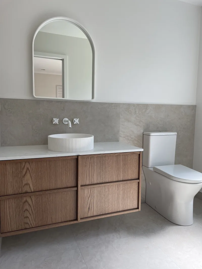 Newly finished bathroom with a wall-hung oak vanity, round basin, arched mirror and grey stone-look tiles