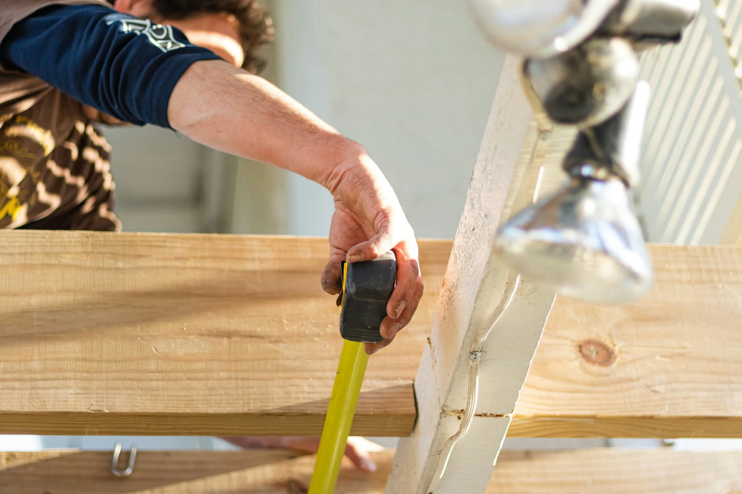 Close-up of a builder's hand running a tape measure along a length of framing timber