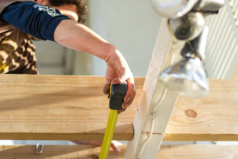 Close-up of a builder's hand running a tape measure along a length of framing timber