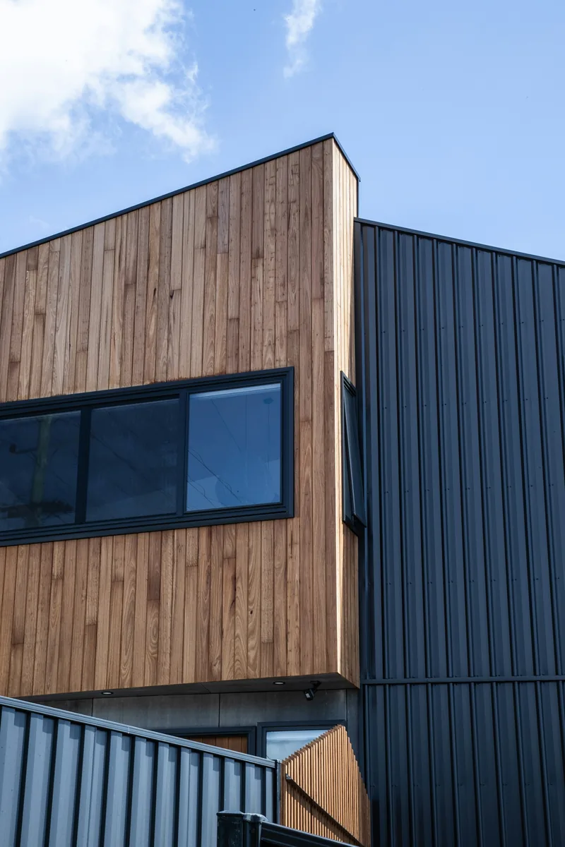 Exterior of a two-storey home reclad in vertical cedar weatherboards and black standing-seam metal, seen against a blue sky