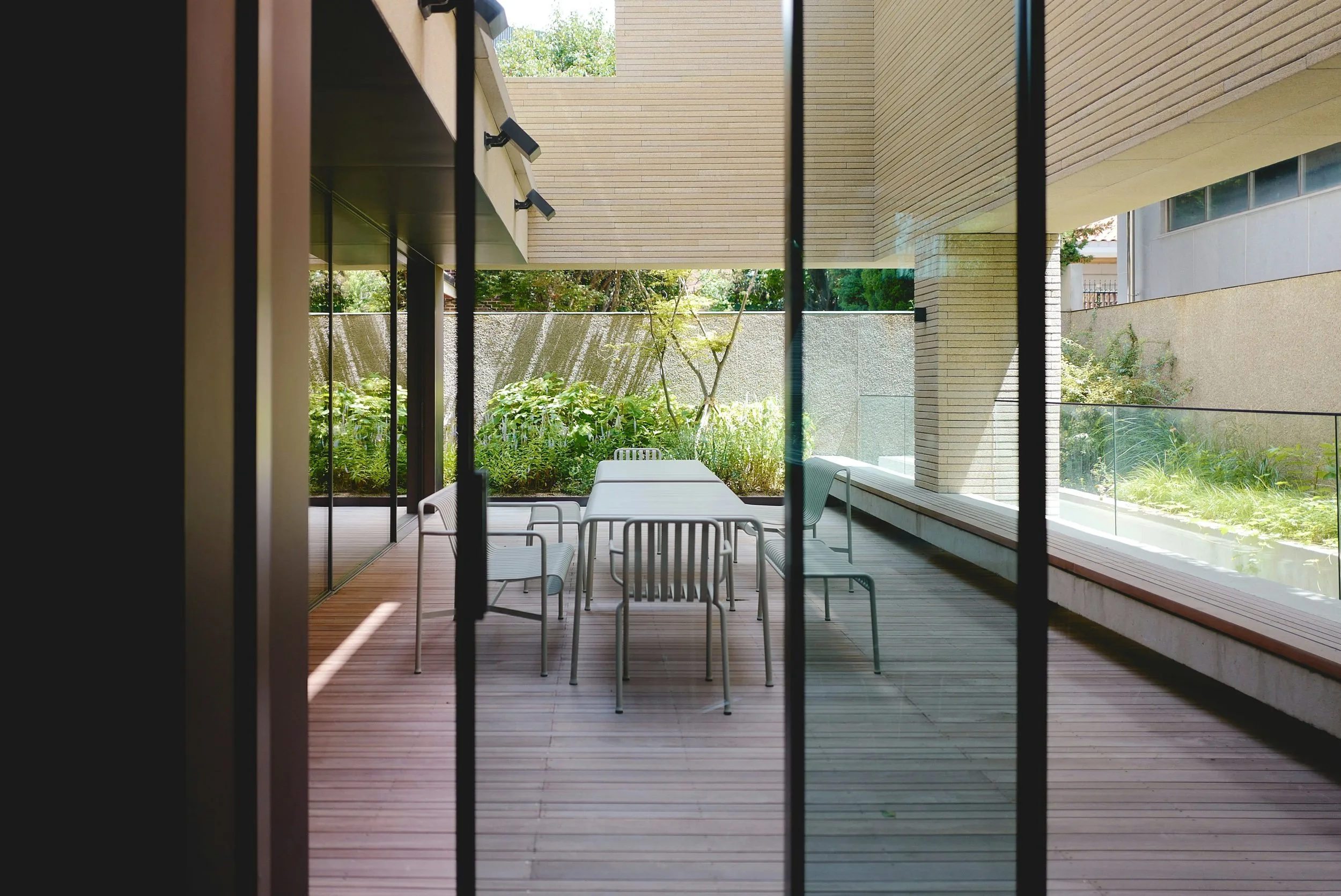 Covered timber deck with an outdoor dining table and chairs, opening from full-height glass sliders onto a planted courtyard