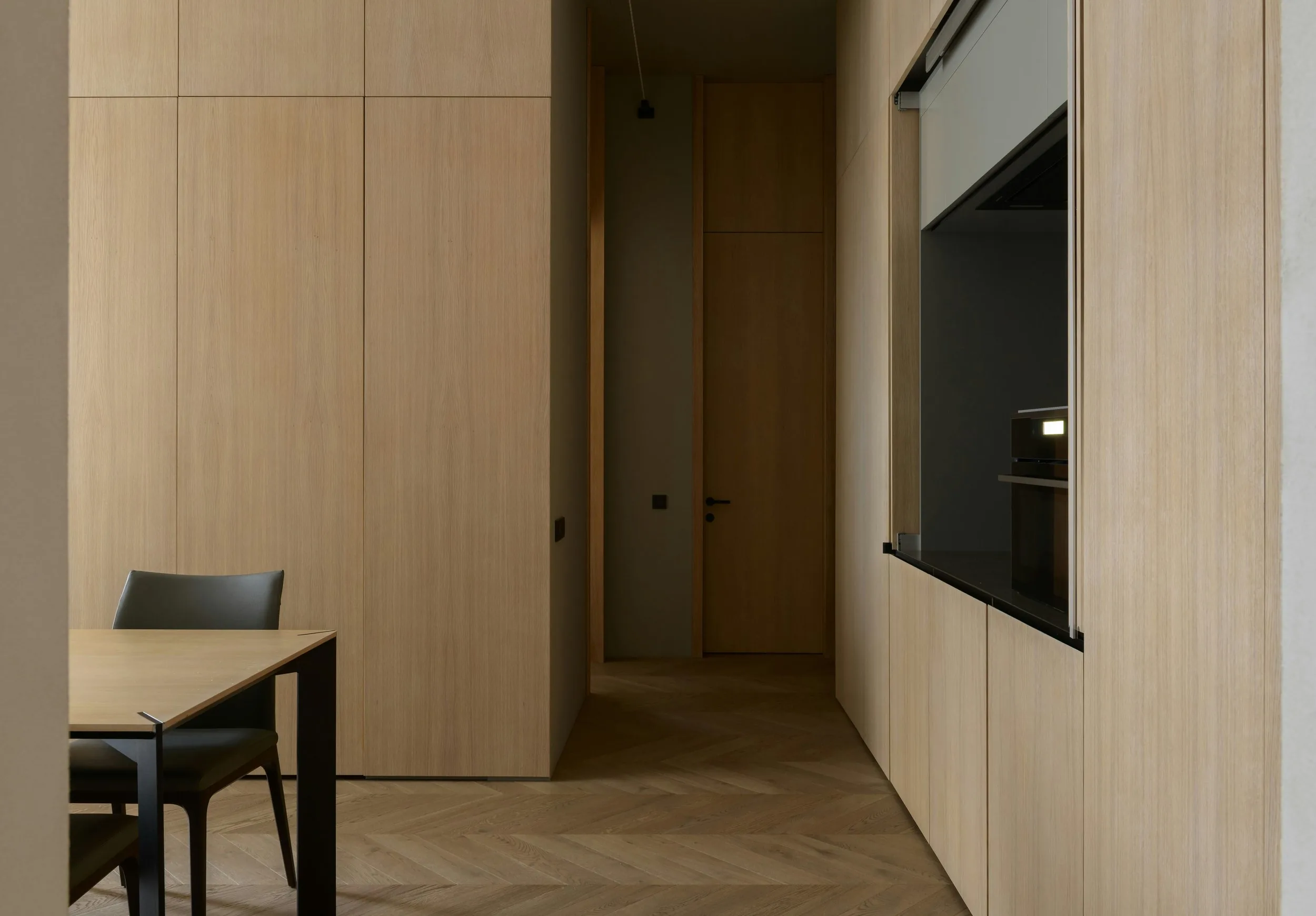 Light oak-panelled hallway and built-in joinery in a modern home interior, with a dining table and black chair in the foreground